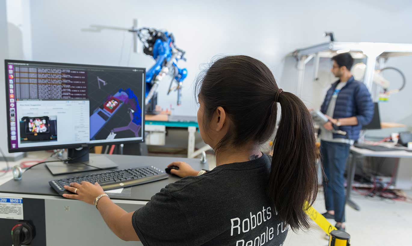 A woman at PlusOne Robotics works on programming on a computer.